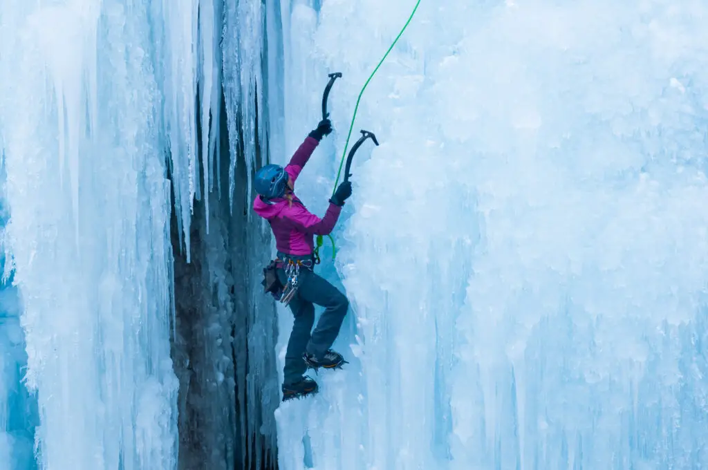 athletic woman in pink coat climbing ice in ouray, colorado